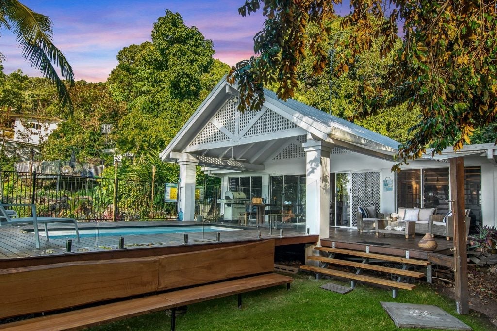 Modern white home with pool, deck, and landscaping surrounded by trees at sunset